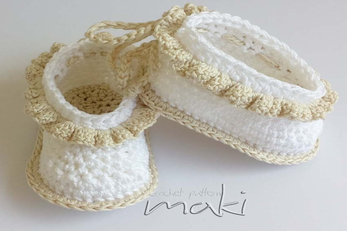 White slip-on crochet baby booties with a yellow ruffle around the top and a matching yellow sole.
