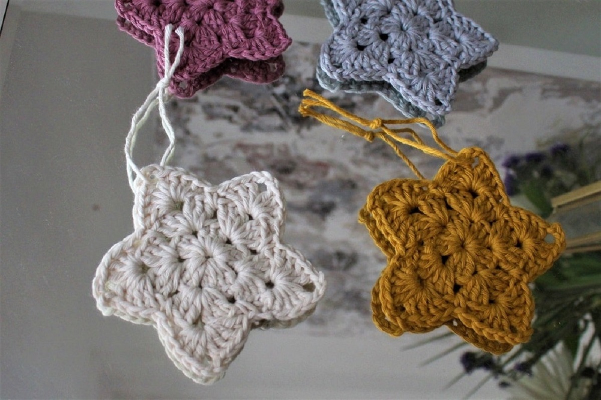 Small white, yellow, blue, and purple crochet Christmas stars with strings attached for you to hang them up.