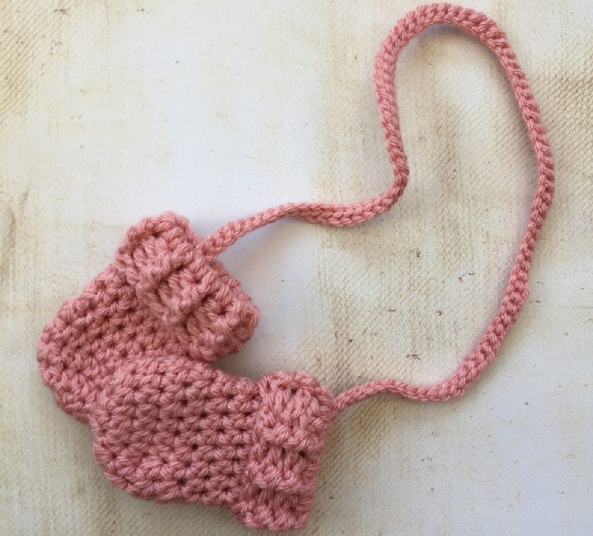 Chunky crochet pink baby mittens attached to a braided string on a white background.