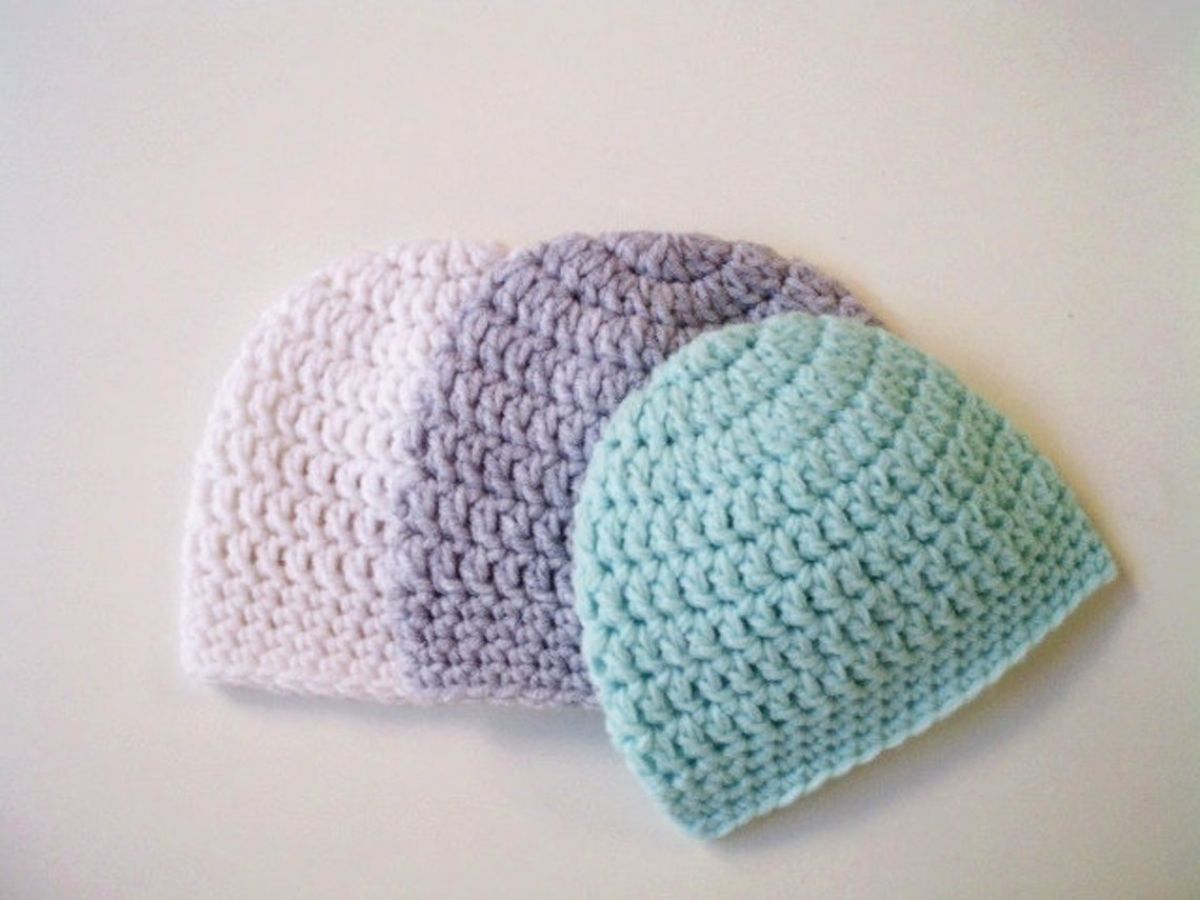 Mint green, purple, and pale pink crochet baby beanie hats lying on a white background. 