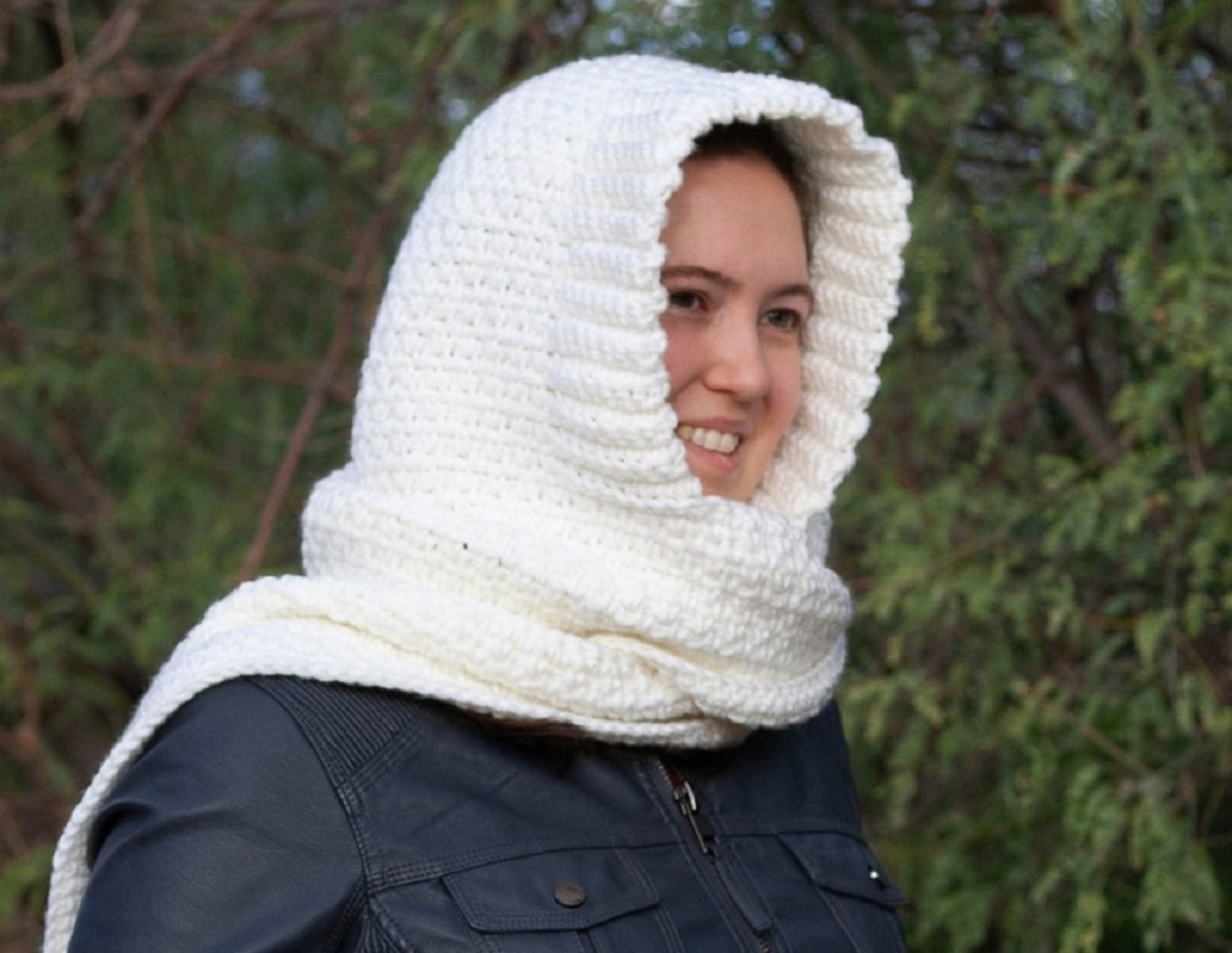 Brunette woman standing outside wearing a white crochet hooded scarf and a navy jacket.
