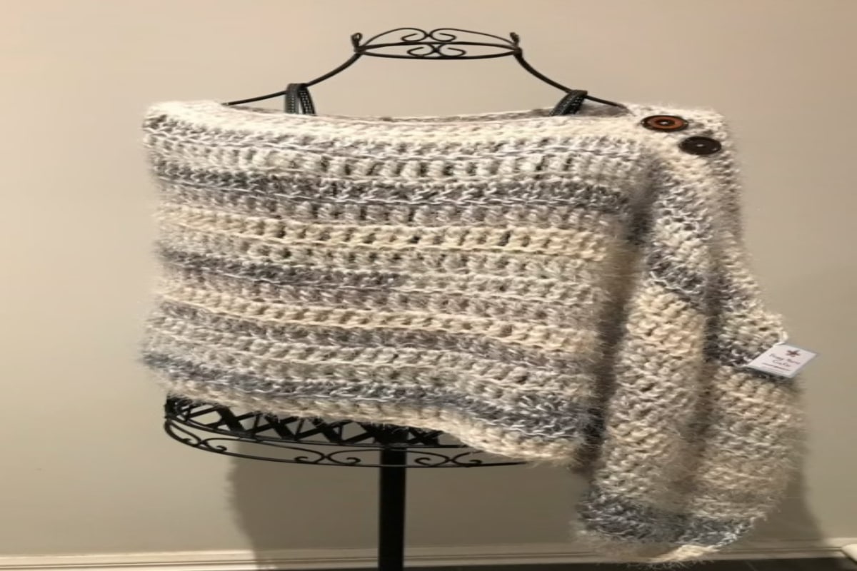 White and grey horizontal striped crochet poncho with black buttons on the right side over a black metal mannequin.