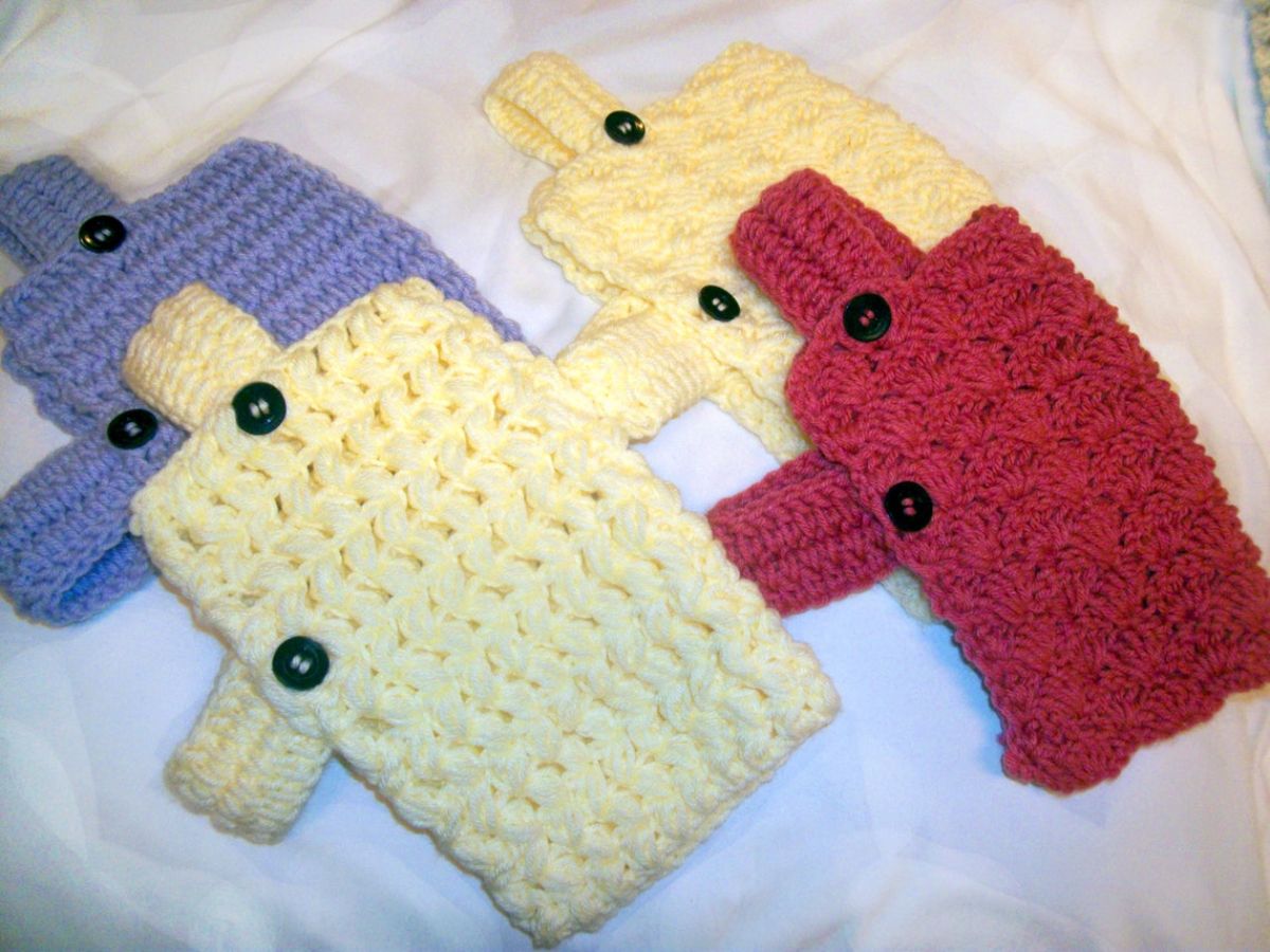 Four small dog sweaters in red, cream, yellow, and blue with black buttons and a band to fasten across the stomach on a white background. 