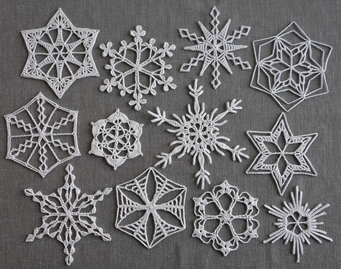 Various white crochet snowflakes in different shapes and sizes spread across a gray background.