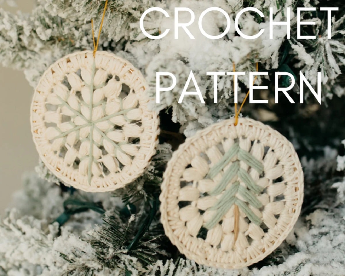 Two round white crochet snowflake ornaments with a green Christmas tree in the center hanging from a snowy Christmas tree.