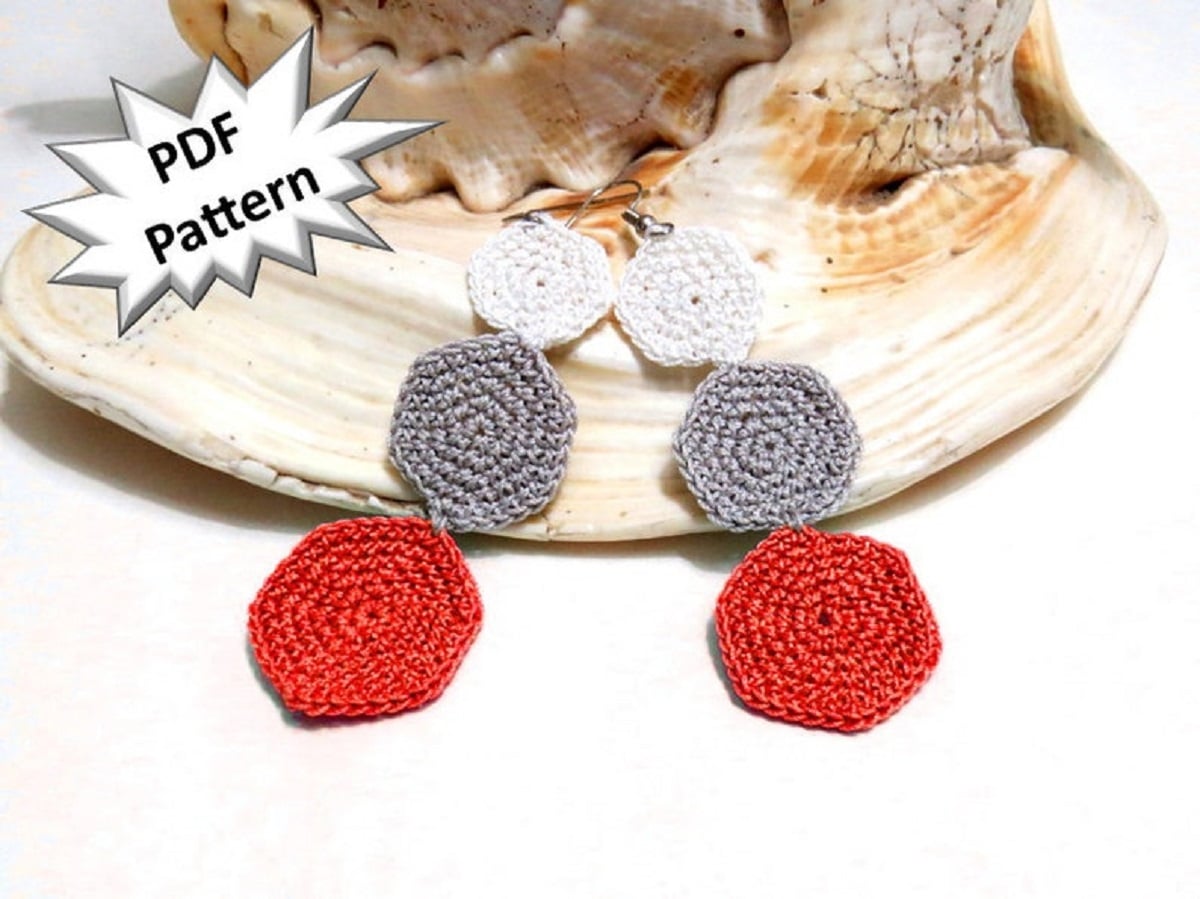A pair of crochet earrings with cream, gray, and red hexagons getting larger in size at the bottom of the earrings.