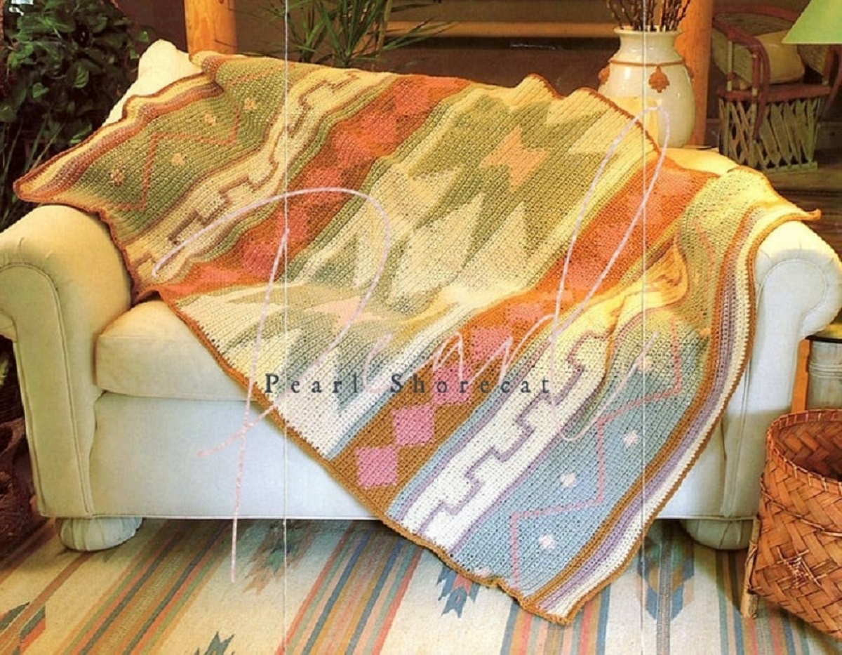 Green, orange, and blue horizontal striped blanket with zig-zags and Native American designs draped over a white sofa.