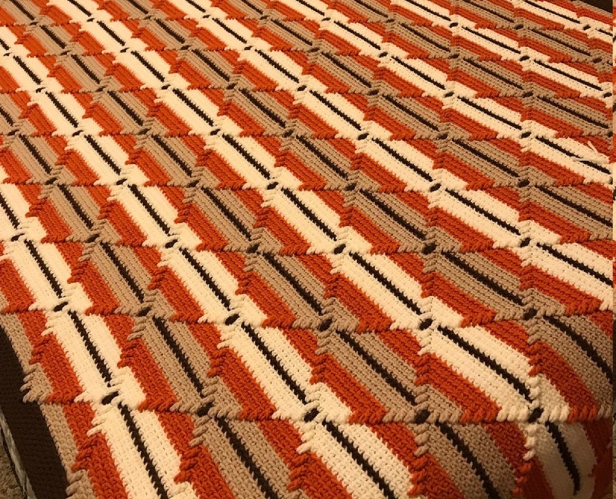 Brown, orange, black, and yellow horizontal stripes with a diamond stitch crochet on the top of this Navajo blanket. 
