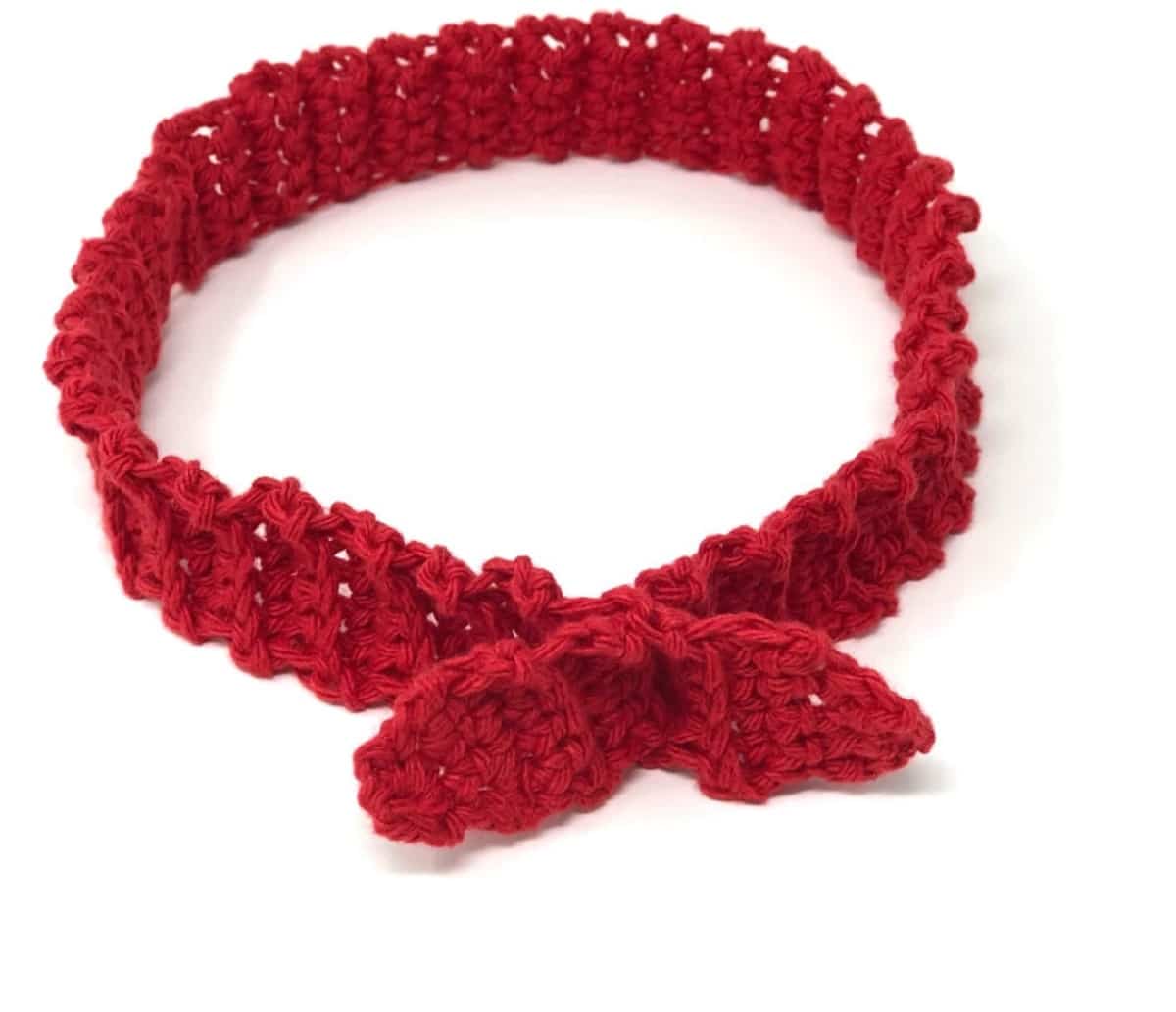 Slim red crochet headband with a small bow in the center on a plain white background.