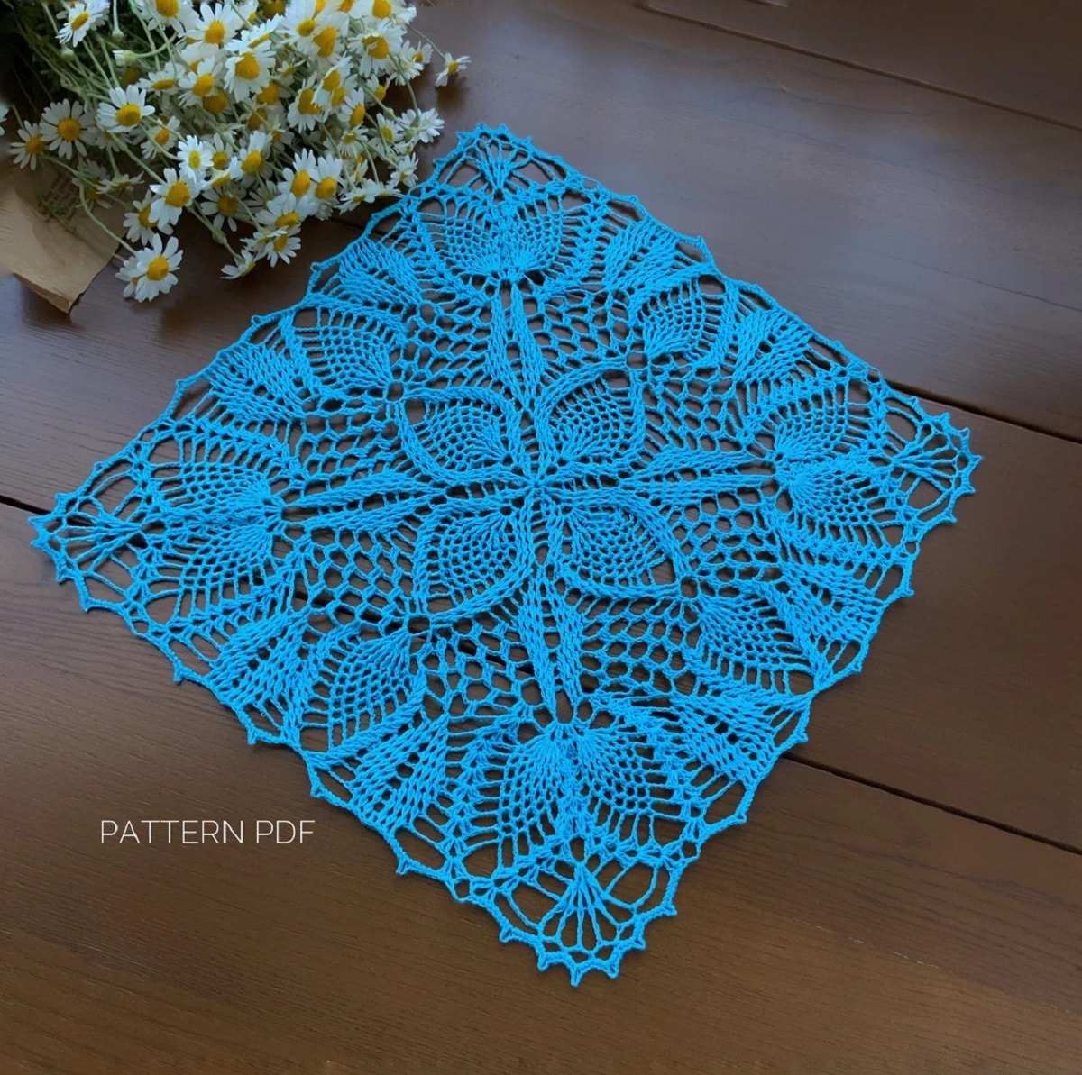 Blue square crochet doily with four pineapples in a petal in the center and pineapples in petals around all sides.