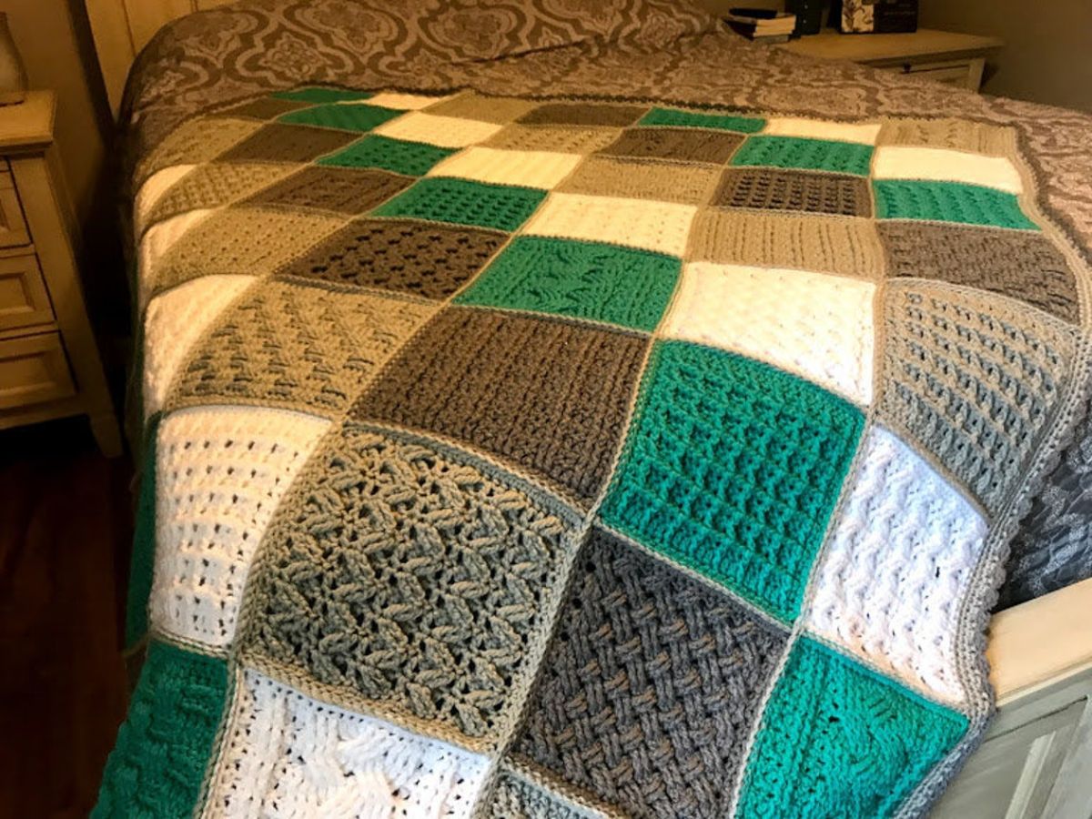 Green, brown, and white patchwork style crochet blanket with waffle stitch and zig zag stitch squares over a large bed.