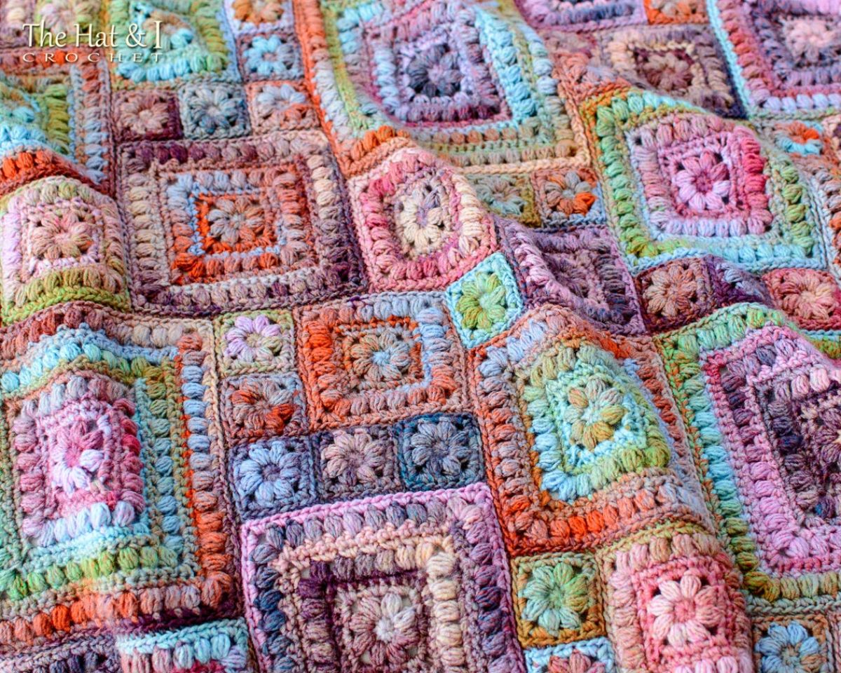 Large patchwork style crochet blanket with multi-colored squares of different sizes with smaller squares or flowers in the center.