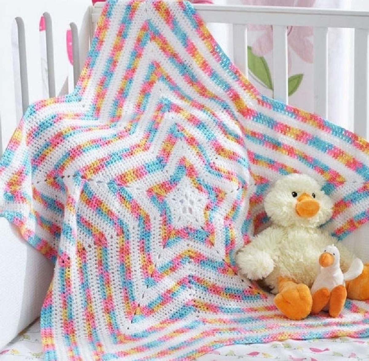 Large pink, blue, and white star shaped blanket with stars decreasing in size as they get closer to the center with a toy duck next to it.