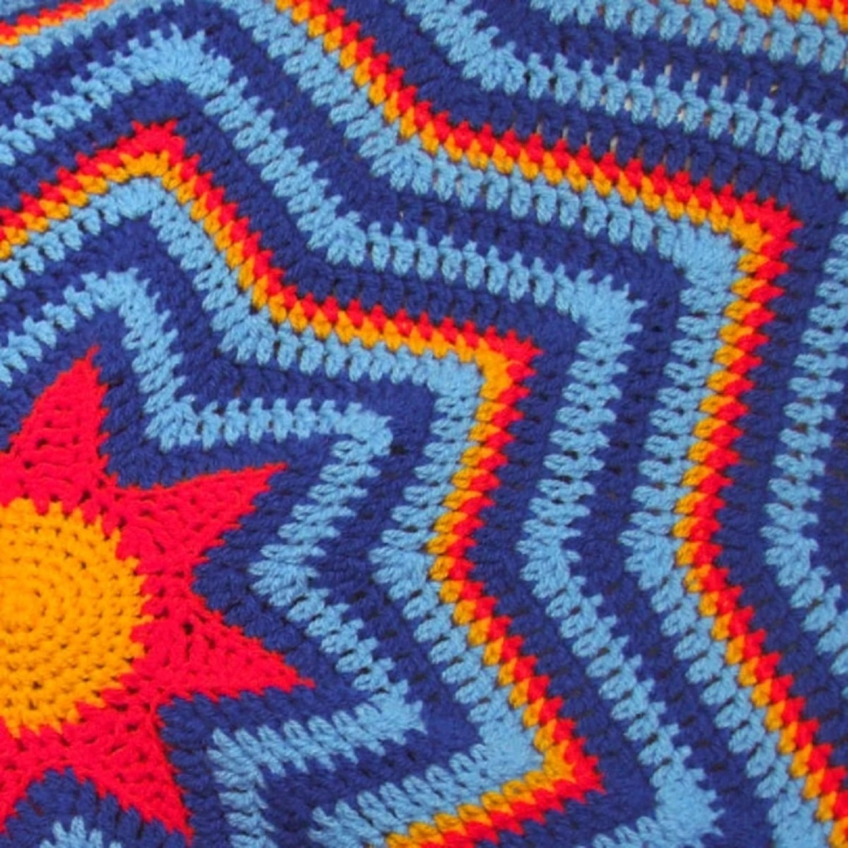 Star shaped crochet blanket with light blue, dark blue, orange, and red stars decreasing in size towards the center.