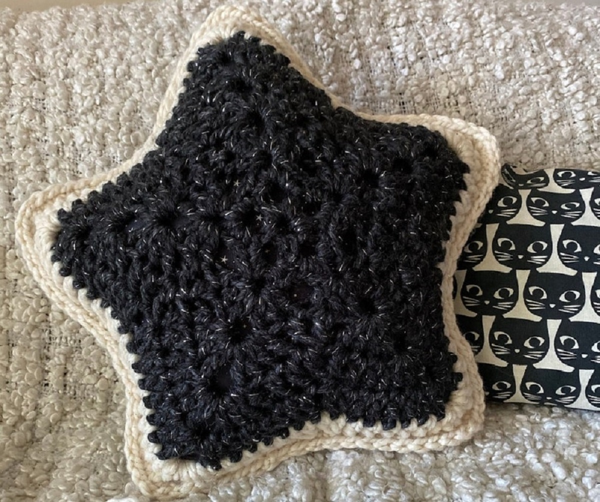 Small black crochet star cushion with a white trim on all sides on top of a cream crochet blanket.