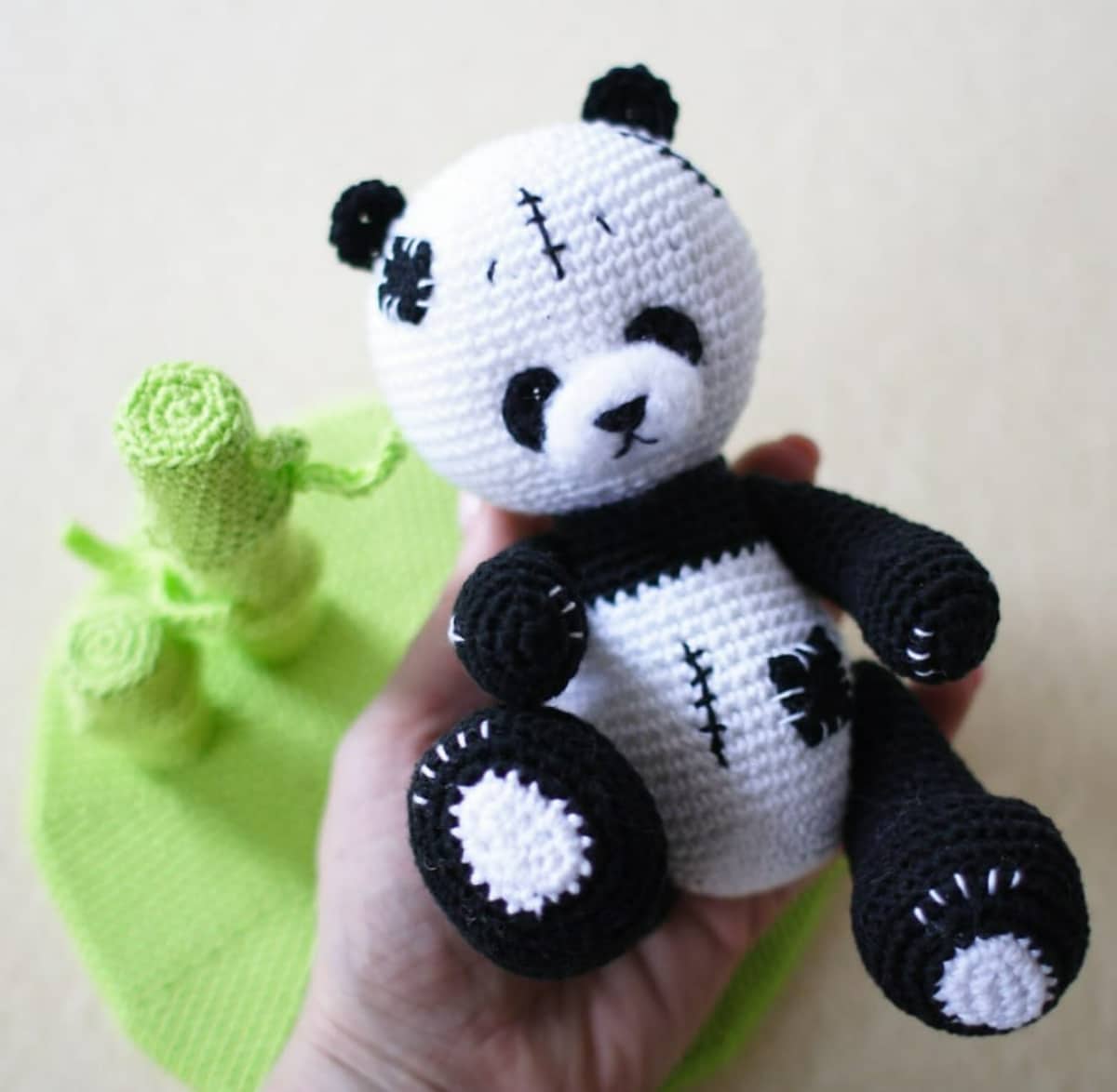 Black and white crochet panda with a black patch stitched on its stomach and stitches on its stomach held next to some green yarn.