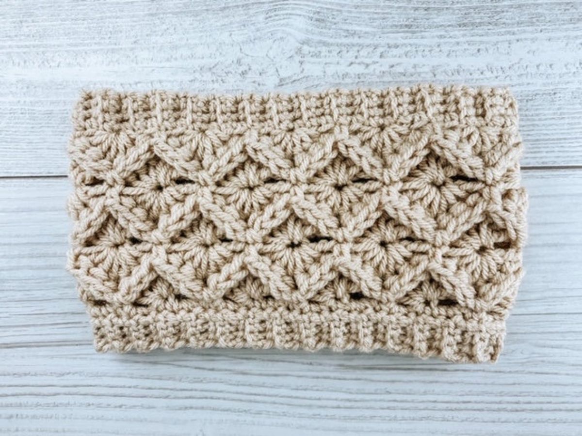 Cream ear warmer with chunky diamond crochet design and narrow trim on a white wooden background.