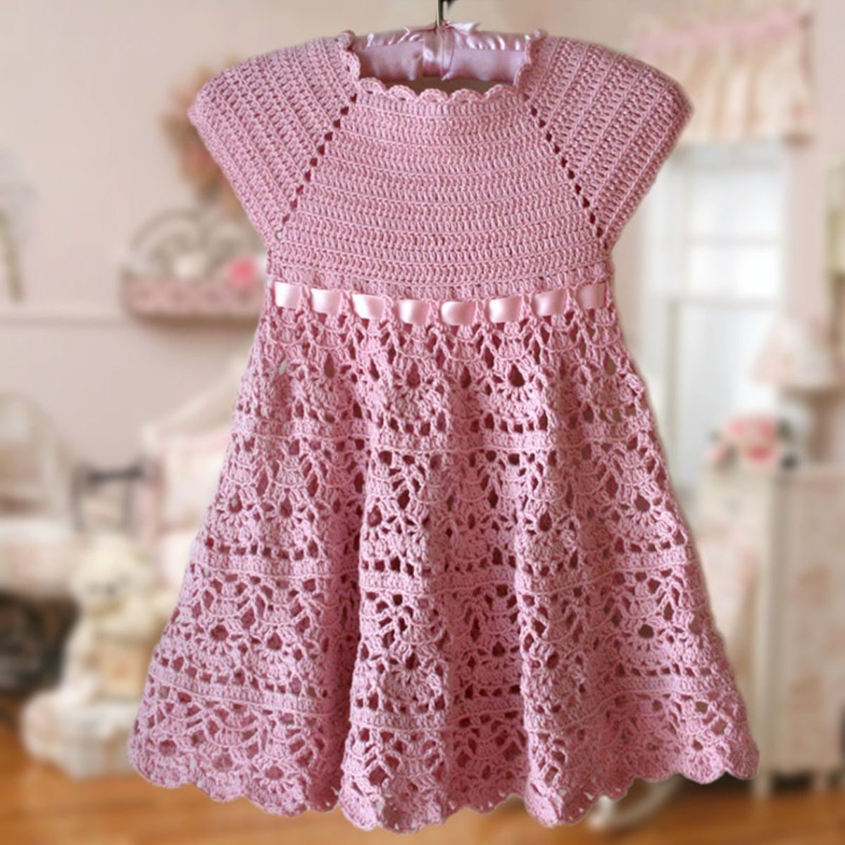 Pink crochet baby dress with a scallop neckline, short sleeves, and a lace style full skirt.