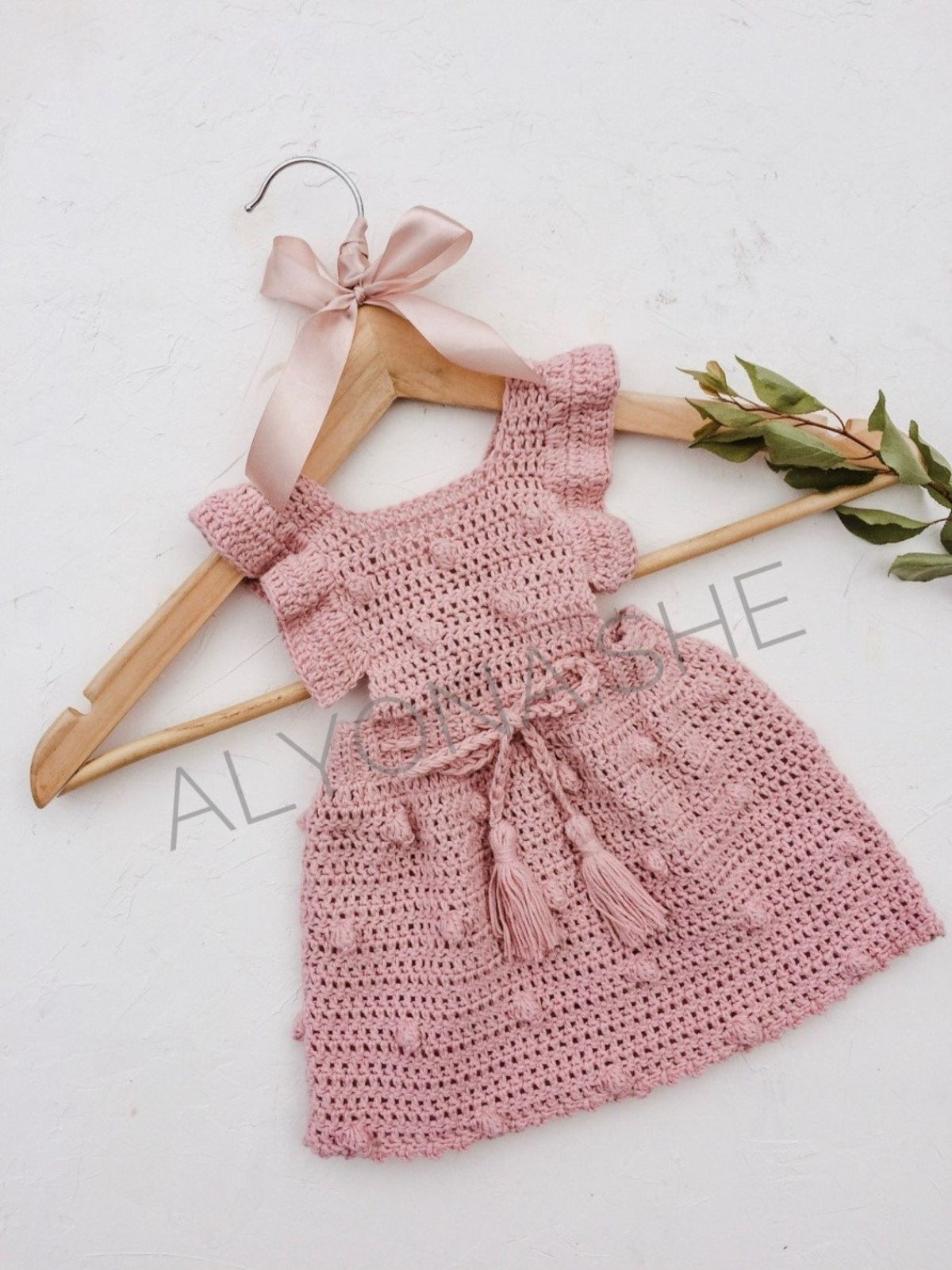 Pink crochet sleeveless baby dress with a ruffle on either strap, a tie around the waist and small bobbles over the whole dress.