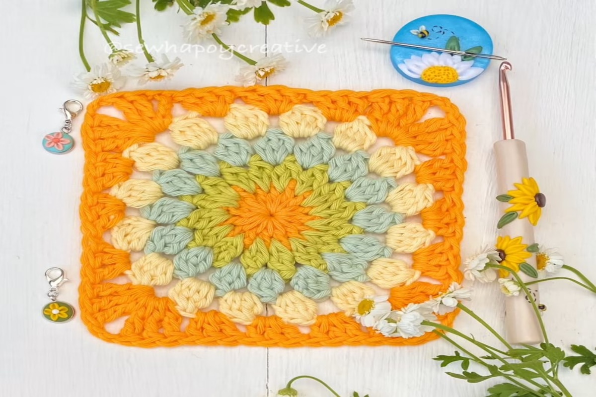 Orange crochet granny square with circles in the center using orange, green, blue, and yellow yarn for each circle.