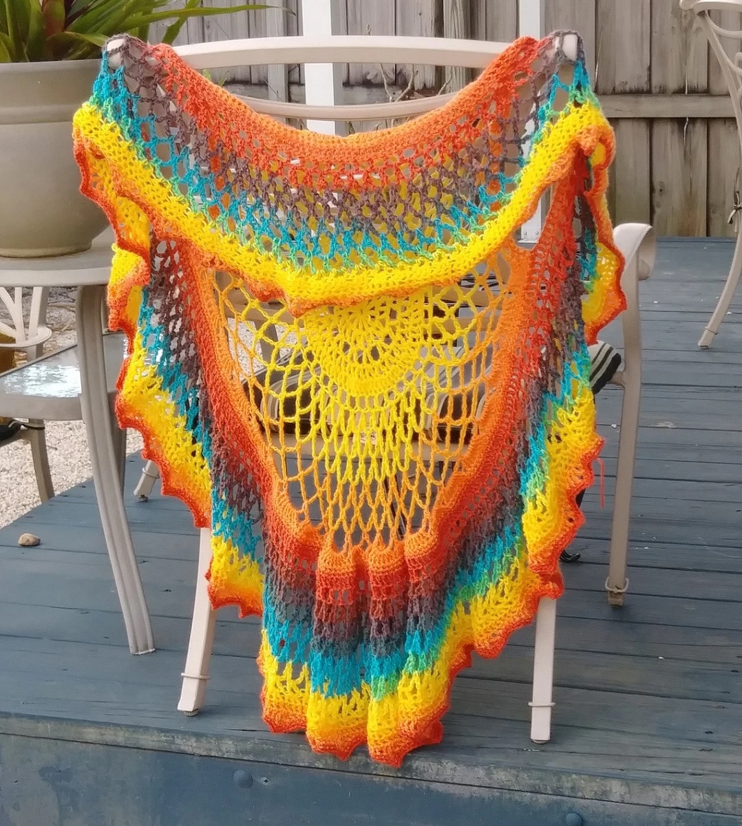 Rainbow colored striped crochet vest with a large yellow mandala in the center draped over the back of a chair.
