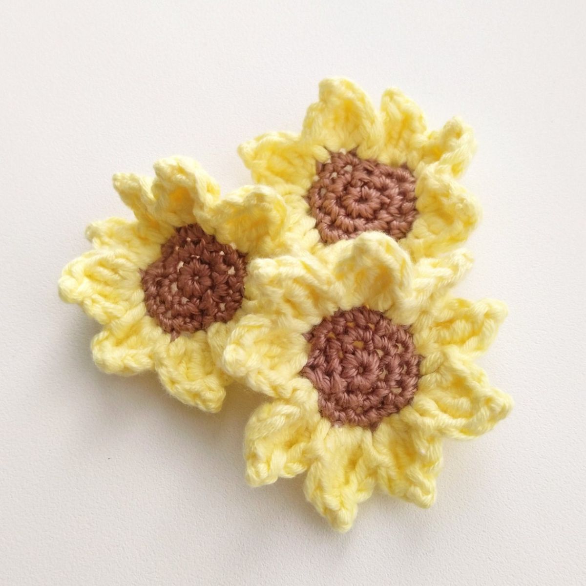Three small crochet yellow and brown sunflowers arranged in a triangle on a white background.