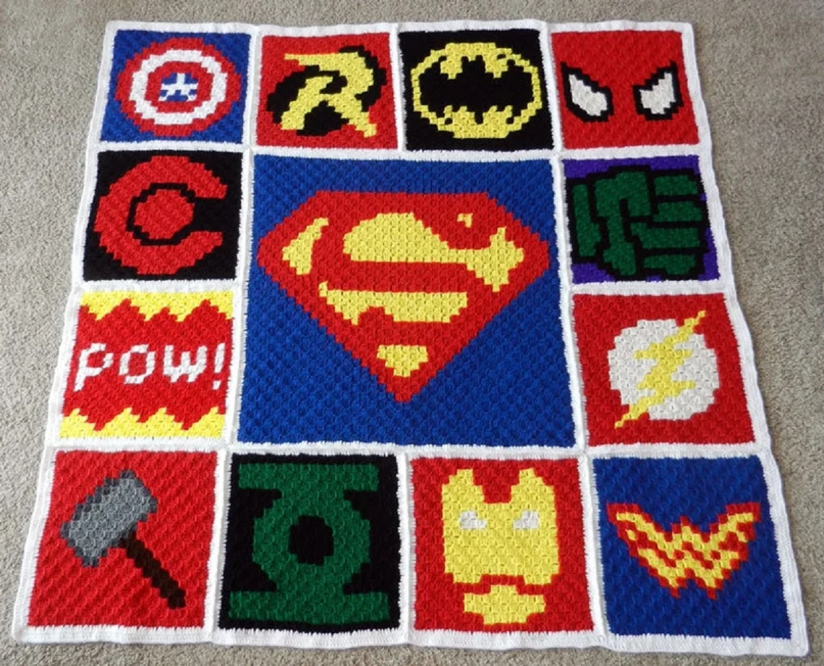  Multi-colored crochet blanket with Marvel and DC superhero logos stitched in squares on a cream background.