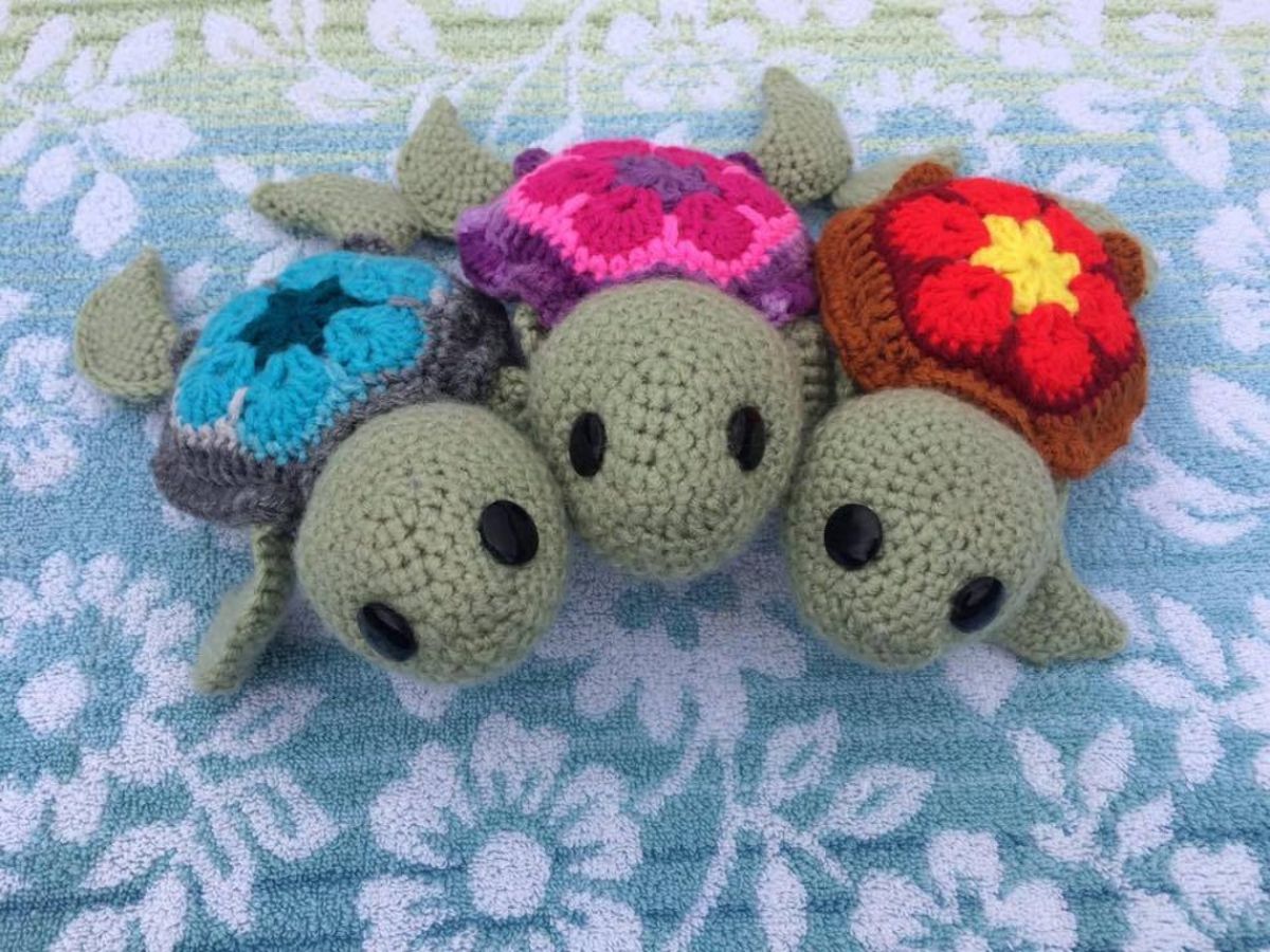 Three small crochet sea turtles with flowers stitched into their shells. One is blue, the other pink and purple, and the third is red and yellow.
