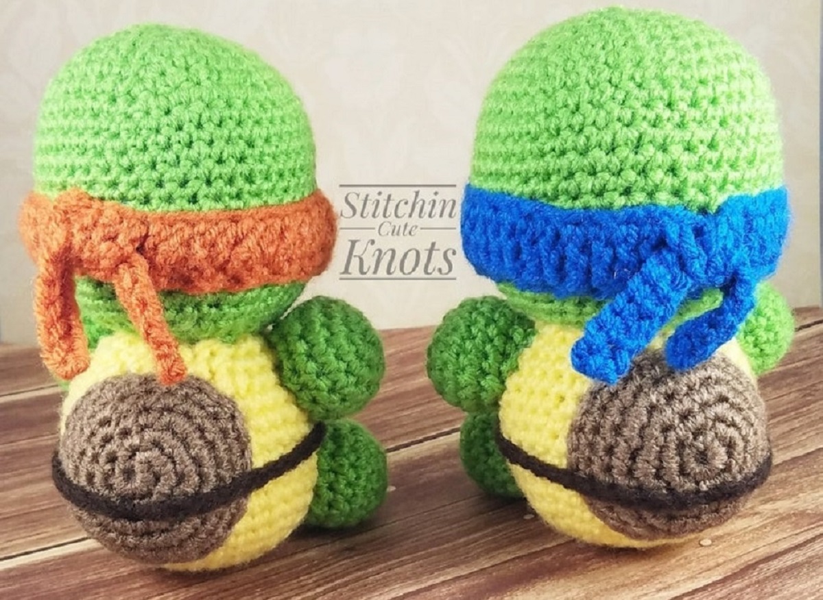 The backs of two green ninja turtles sitting down with yellow and brown shells. Turtles are wearing an orange and blue eye mask. 