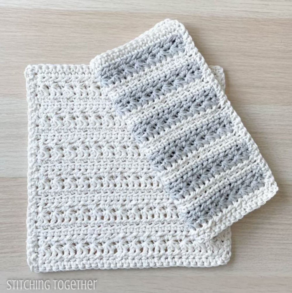A white textured crochet dishcloth with a gray and white striped dishcloth folded in half on top of it.