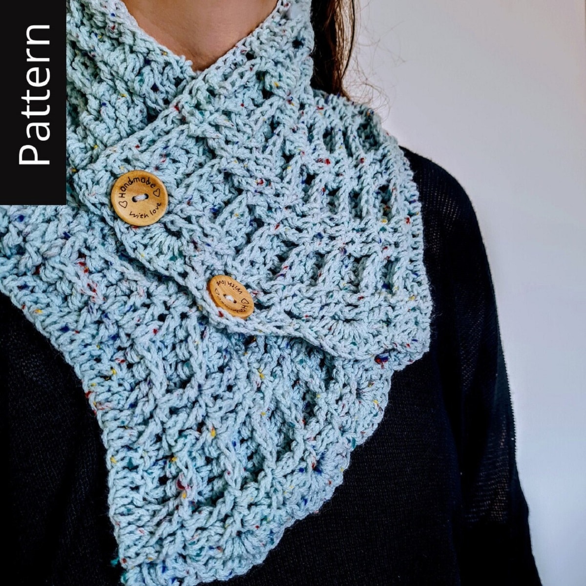 Brunette woman wearing a blue crochet cowl with a loose waffle stitch and brown buttons on the side to secure it.