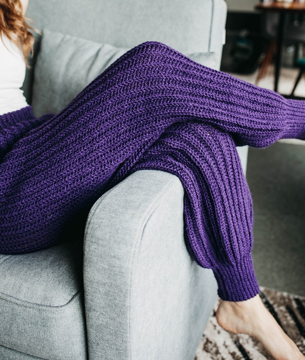 Deep purple crochet baggy trousers with a cuff at the bottom, worn by a woman with her legs over the arm of a couch.