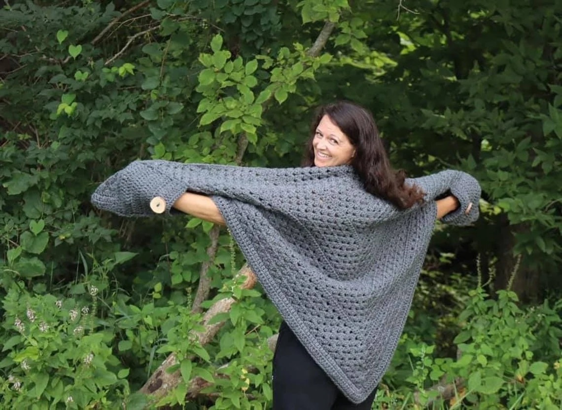 Brunette woman with her head over her shoulder wearing a large gray crochet shawl with white buttons on the sleeves.