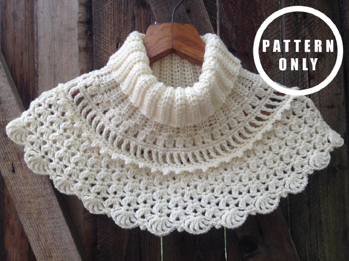 High neck cream crochet cowl with a row of small circles, vertical lines, a flower pattern and a scalloped edging with a fan pattern at the bottom.