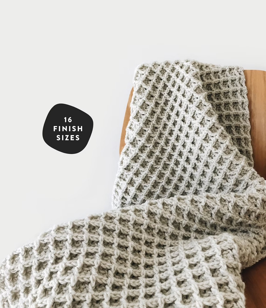Cream waffle stitch crochet blanket folded and draped over a wooden chair next to a white wall.