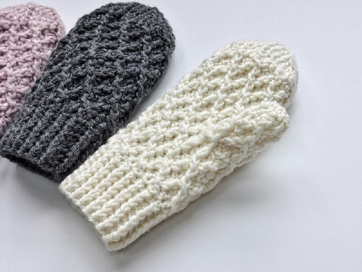 Chunky crochet white, black, and purple mittens lying next to each other on a white background.