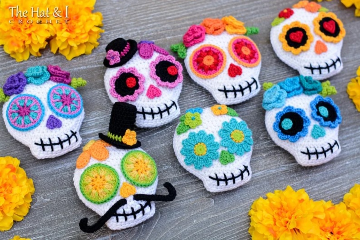 Seven white crochet skulls with a sugar skull pattern on them in bright blue, orange, pink, green, and red.