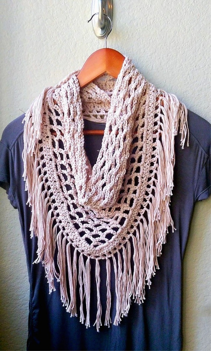  A wooden hanger with a navy blue t-shirt and a pale pink crochet scarf with long pink tassels hanging from it.