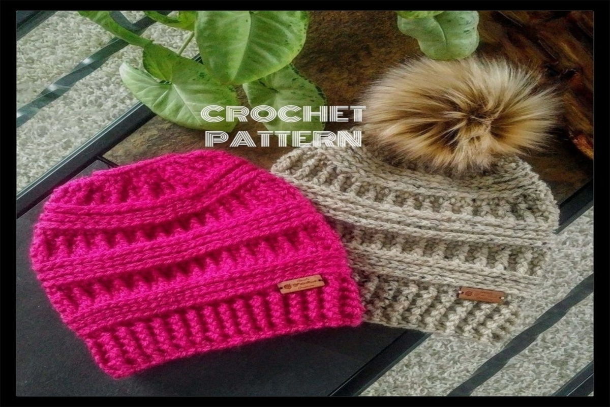 A bright pink crochet hat with thick horizontal lines next to a gray crochet hat with a large brown bobble on the top.