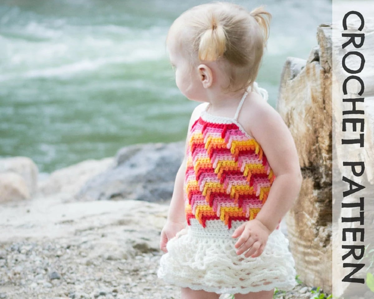 Blond toddler wearing a trail of tears pattern crochet dress with a pink and orange top and white ruffle skirt.