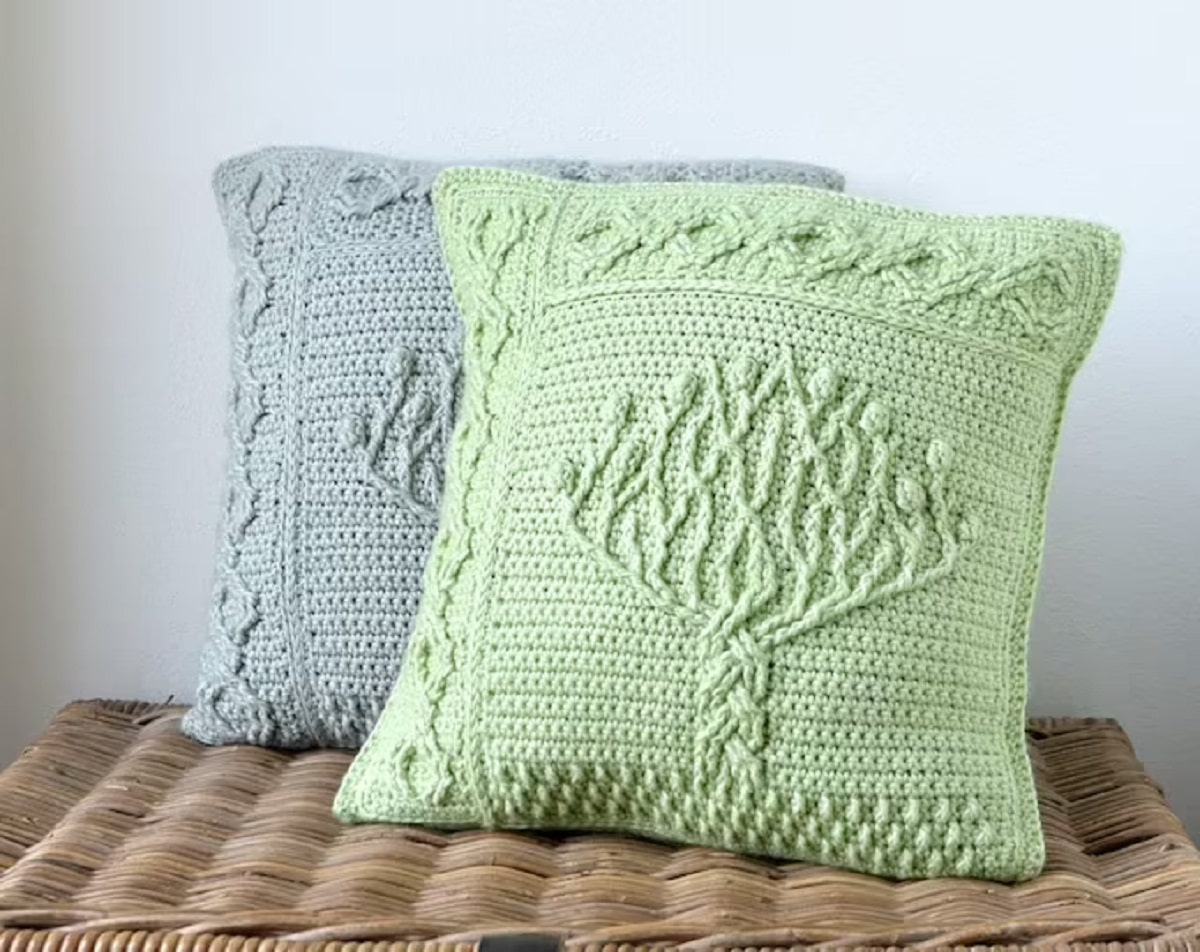 Lime green and pale green crochet cushions next to each other with a tree of life stitched into the center in the same color.