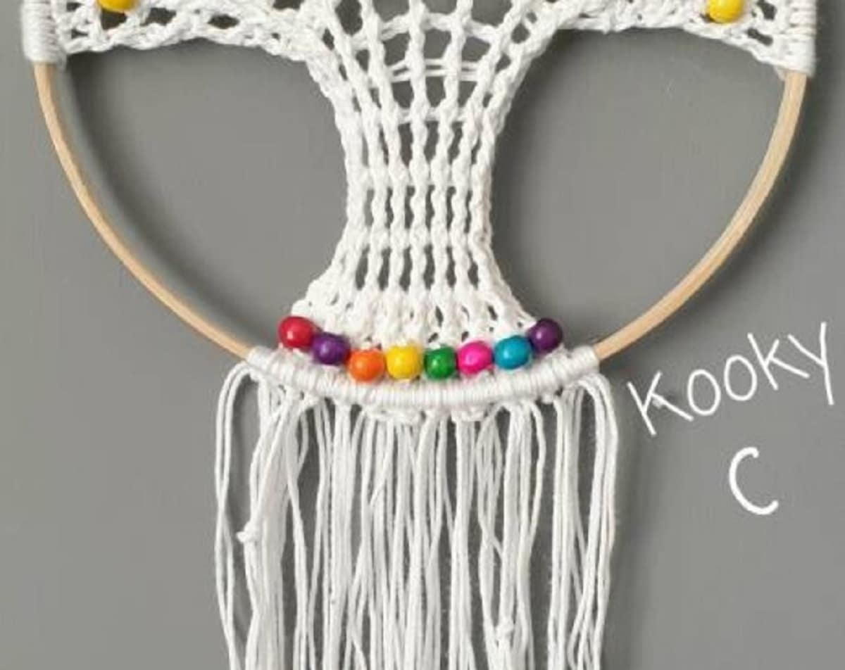 Cream crochet tree of life in a wooden hoop with rainbow colored beads at the bottom and yarn hanging down the center of the hoop.