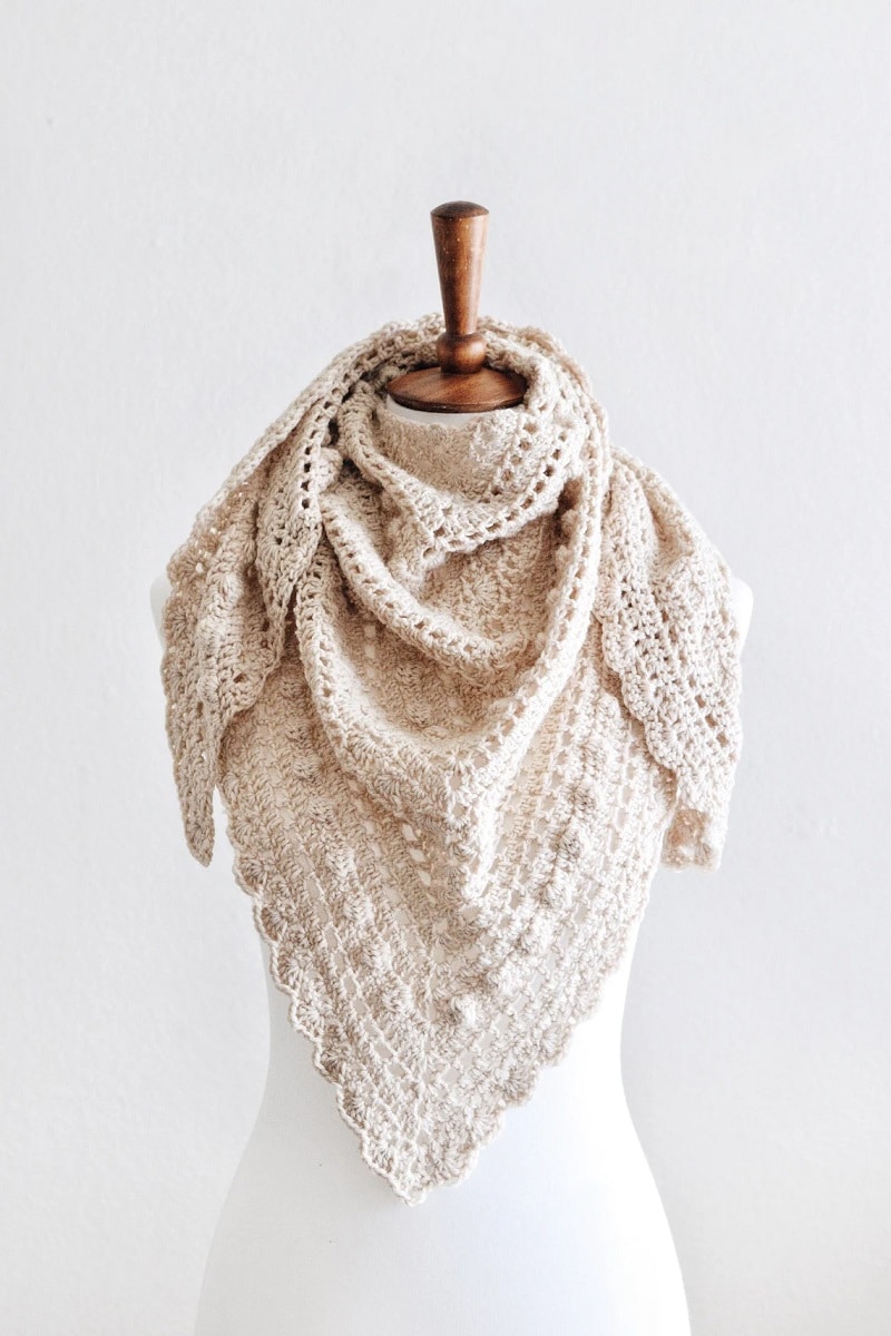 White mannequin wearing a cream crochet triangle lacy scarf with small white bobbles in a diagonal line.