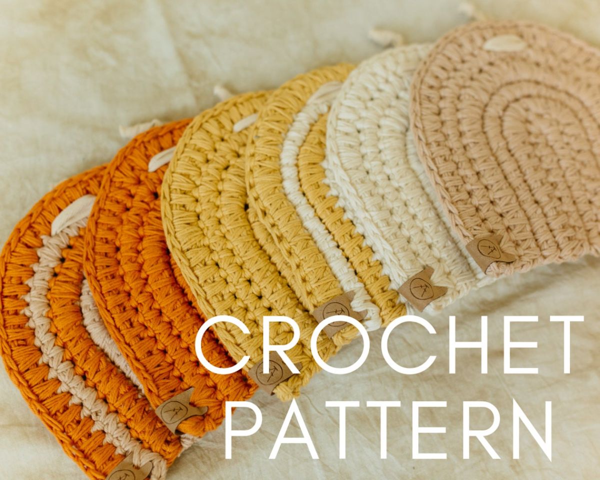 A small pile of pale pink, white, yellow, and orange oval shaped crochet pot holders spread on a white background.