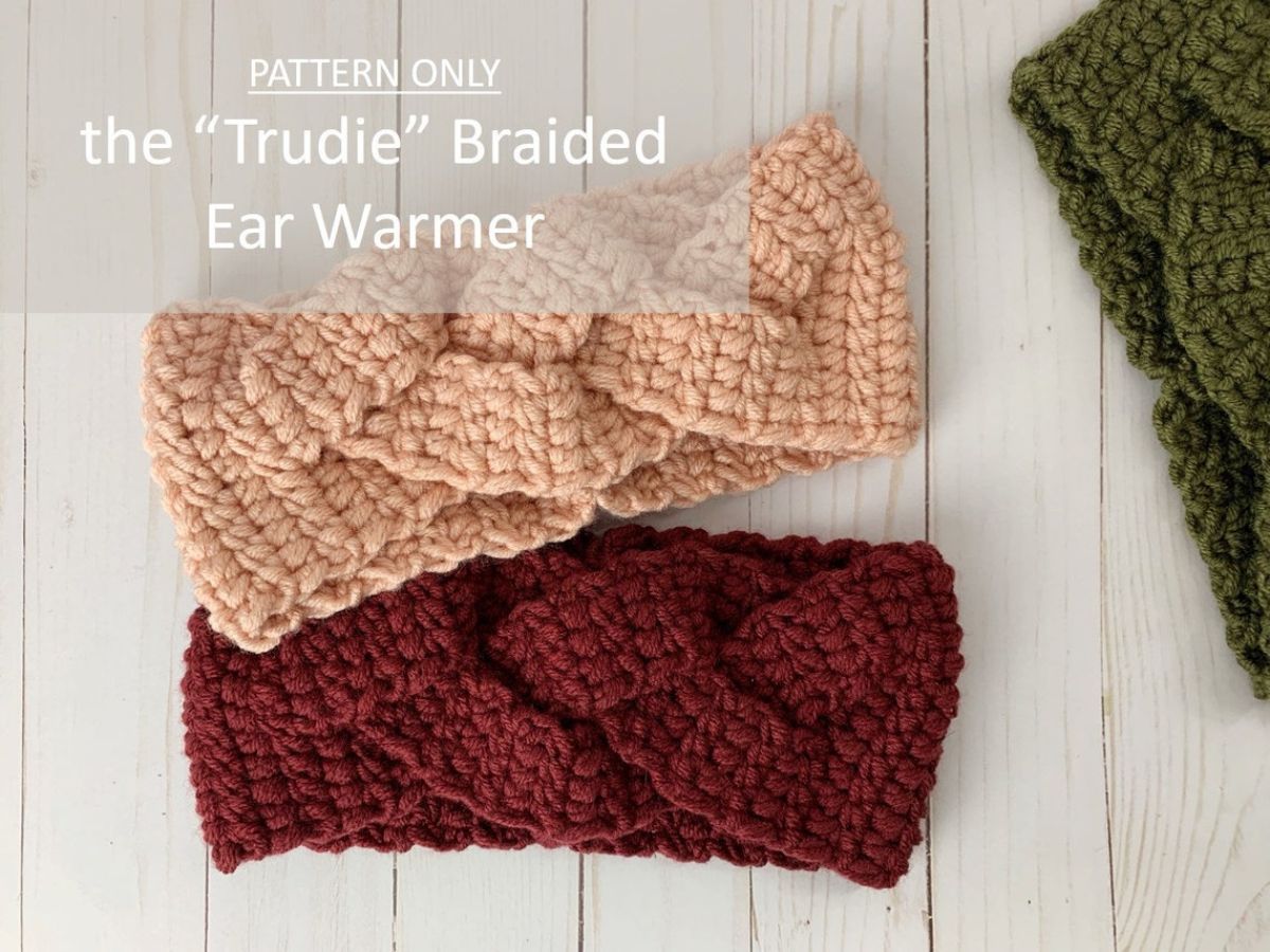 Pale pink and maroon ear warmers with braided design along the front on a white wooden background with a green warmer in the right corner. 