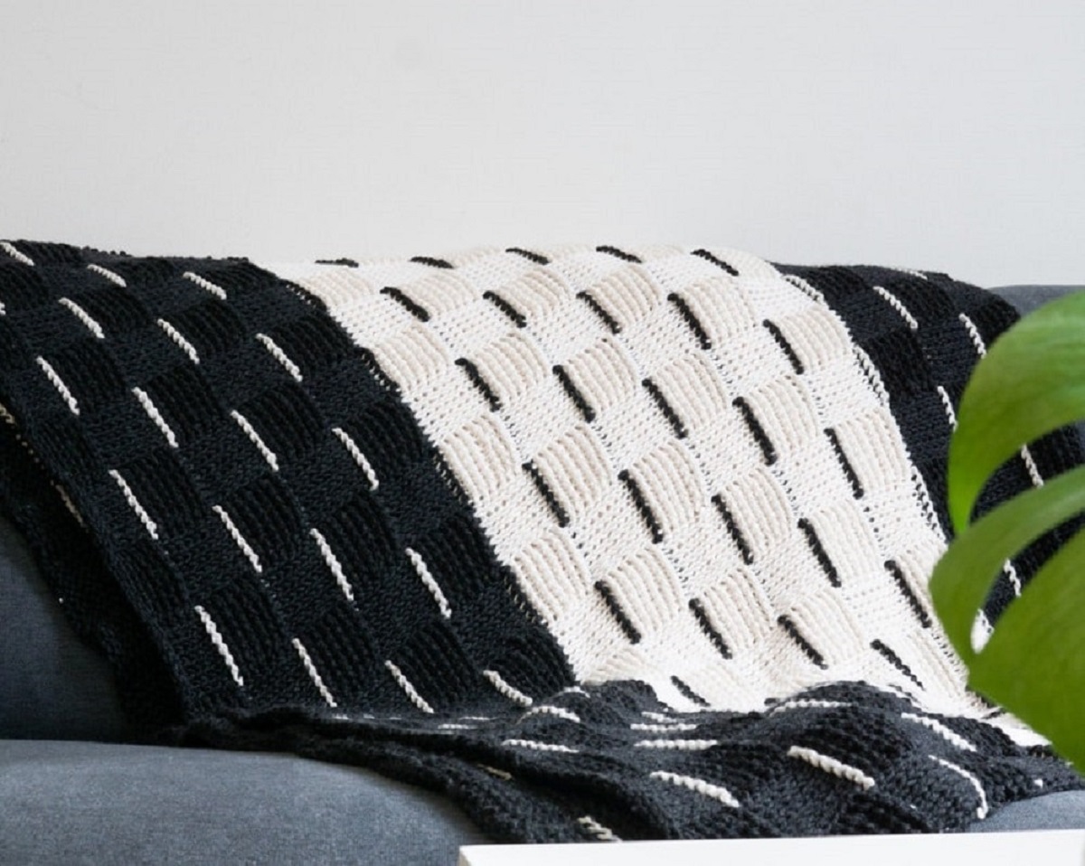 Black and white vertical striped crochet Afghan with white and black lines down each stripe folded over a gray couch.