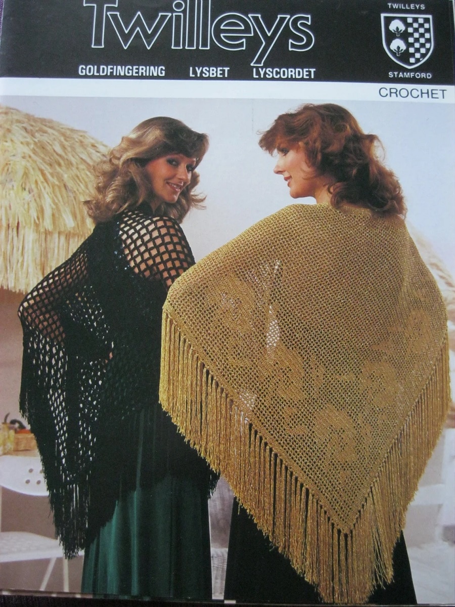 Two women wearing vintage style crochet ponchos. One is black with a loose weave and the other a golden color with long tassels.