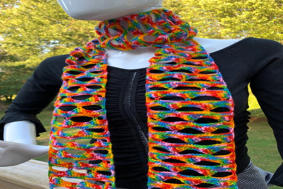 A white mannequin wearing a Billie Holiday style rainbow colored crochet scarf wrapped around its neck.