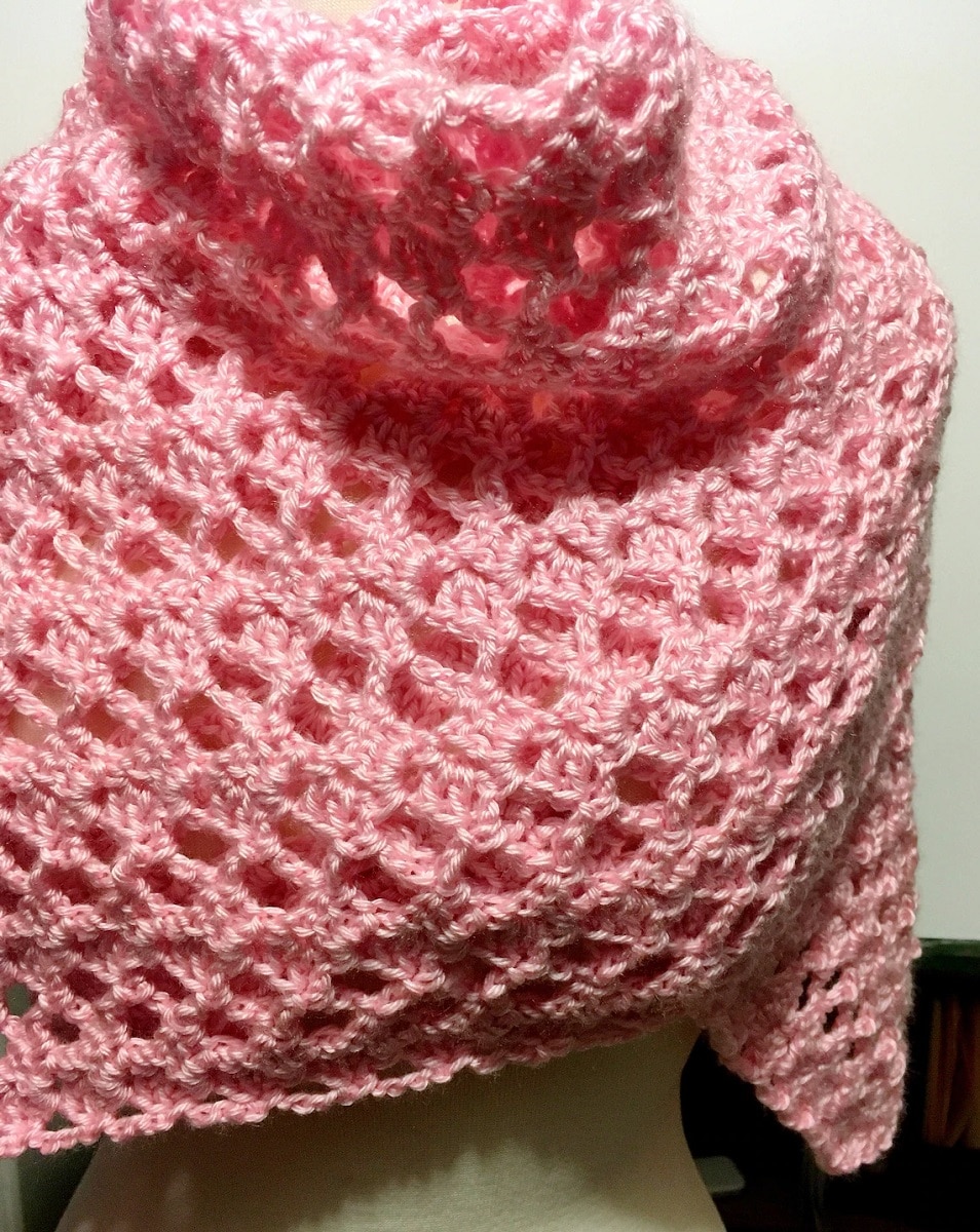 White mannequin wearing a pink lacy crochet shawl around its neck and chest.