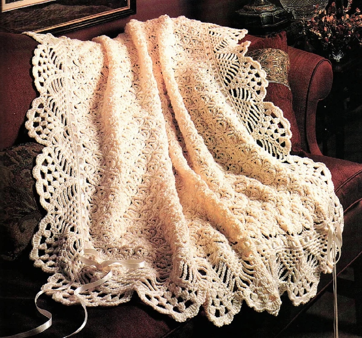 Victorian style lace crochet afghan in pale pink with cream lace trim draped on a maroon sofa.